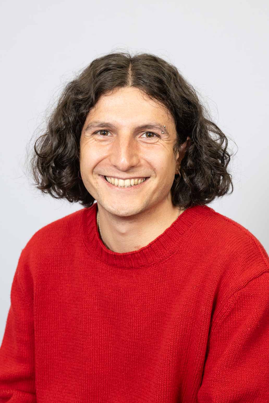 Photo of smiling man with curly hair, wearing a red jumper.